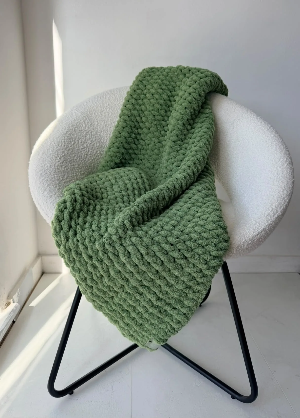 Deep green knitted blanket on a white chair