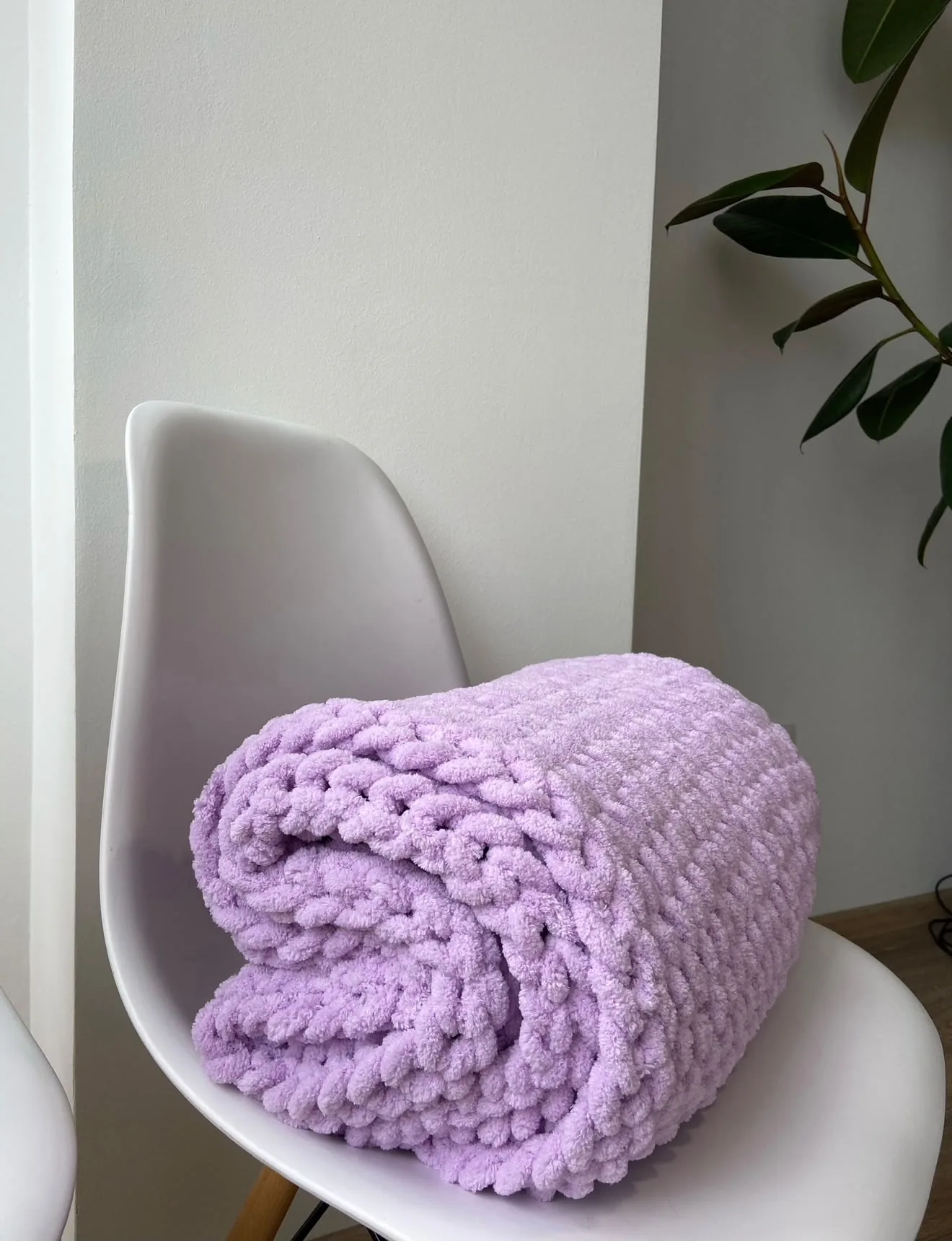 Lilac knitted blanket rolled on a white chair