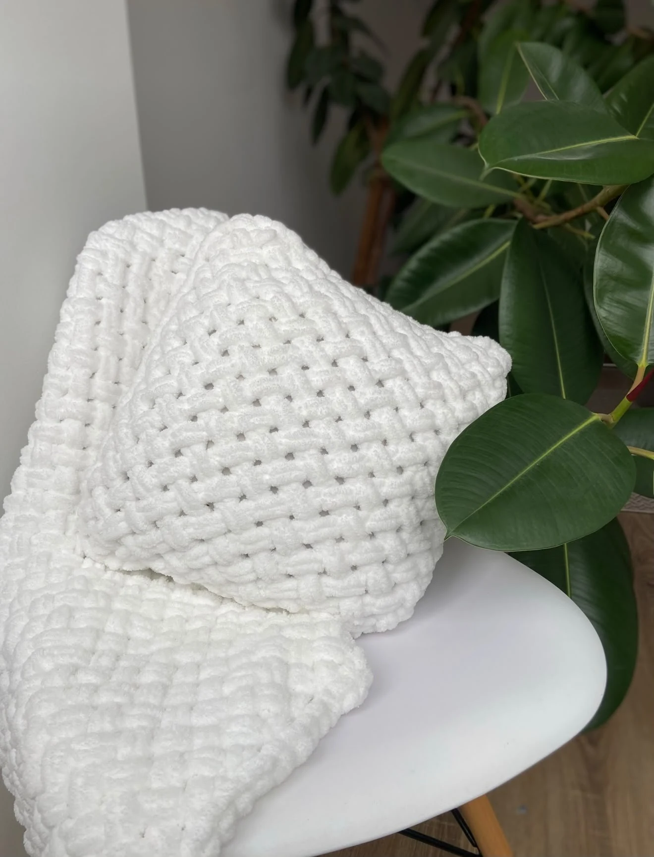 Soft white knitted blanket on a chair beside a green plant